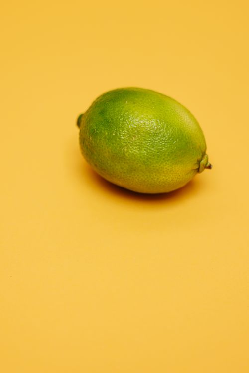Free Close-up of a single fresh green lime on a vibrant yellow background. Stock Photo
