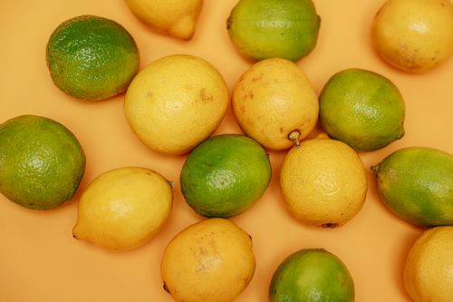 Free Fresh lemons and limes on an orange backdrop, highlighting their vibrant colors. Stock Photo