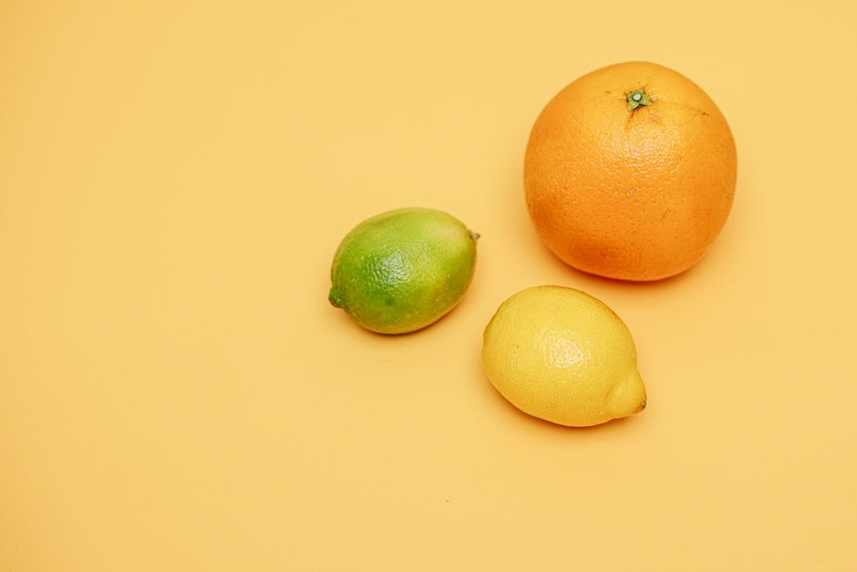 Close-up of lemon, lime, and orange on a yellow surface, showcasing fresh organic citrus fruits.