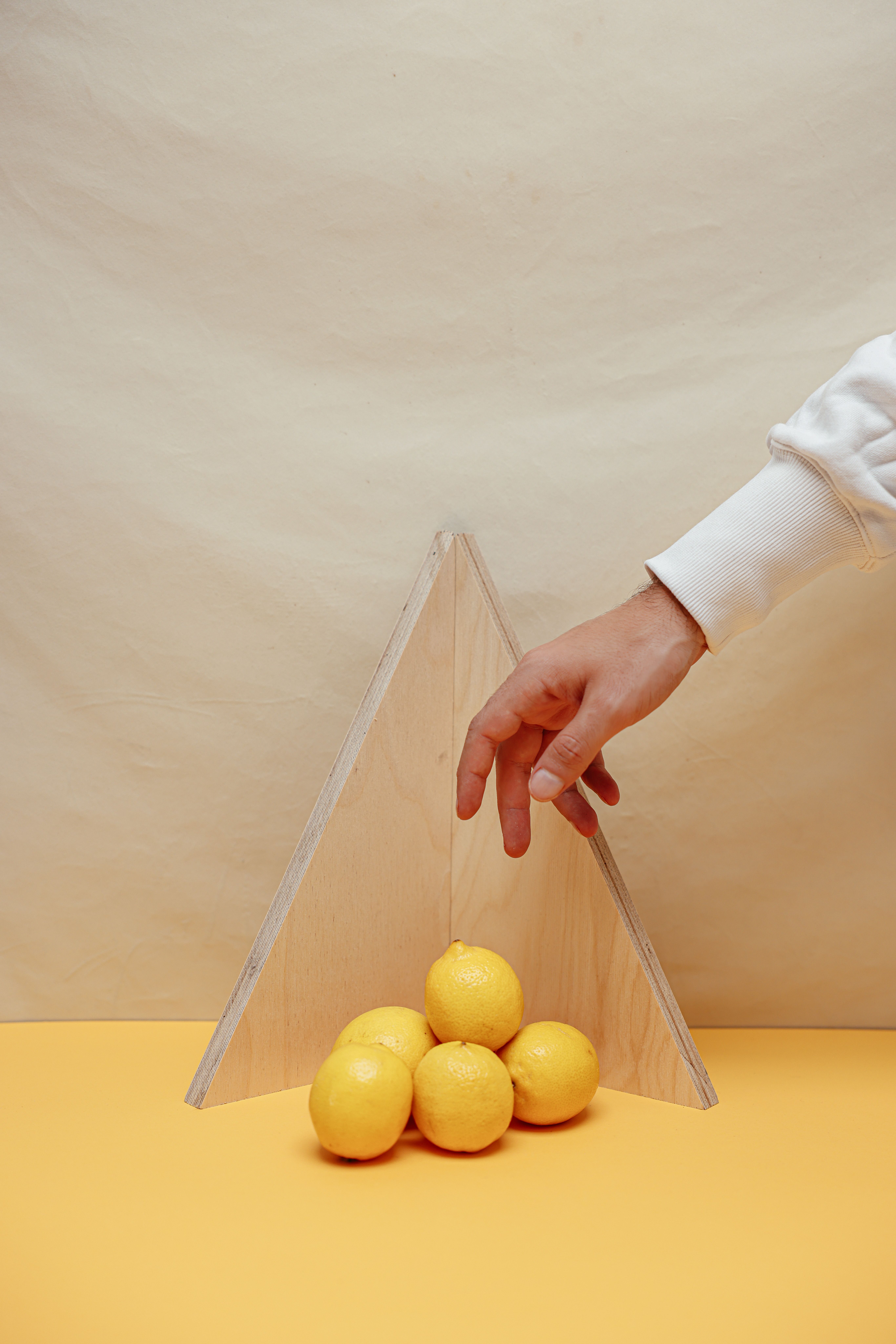 A creative studio shot featuring a hand reaching towards lemons arranged in a triangular setup.