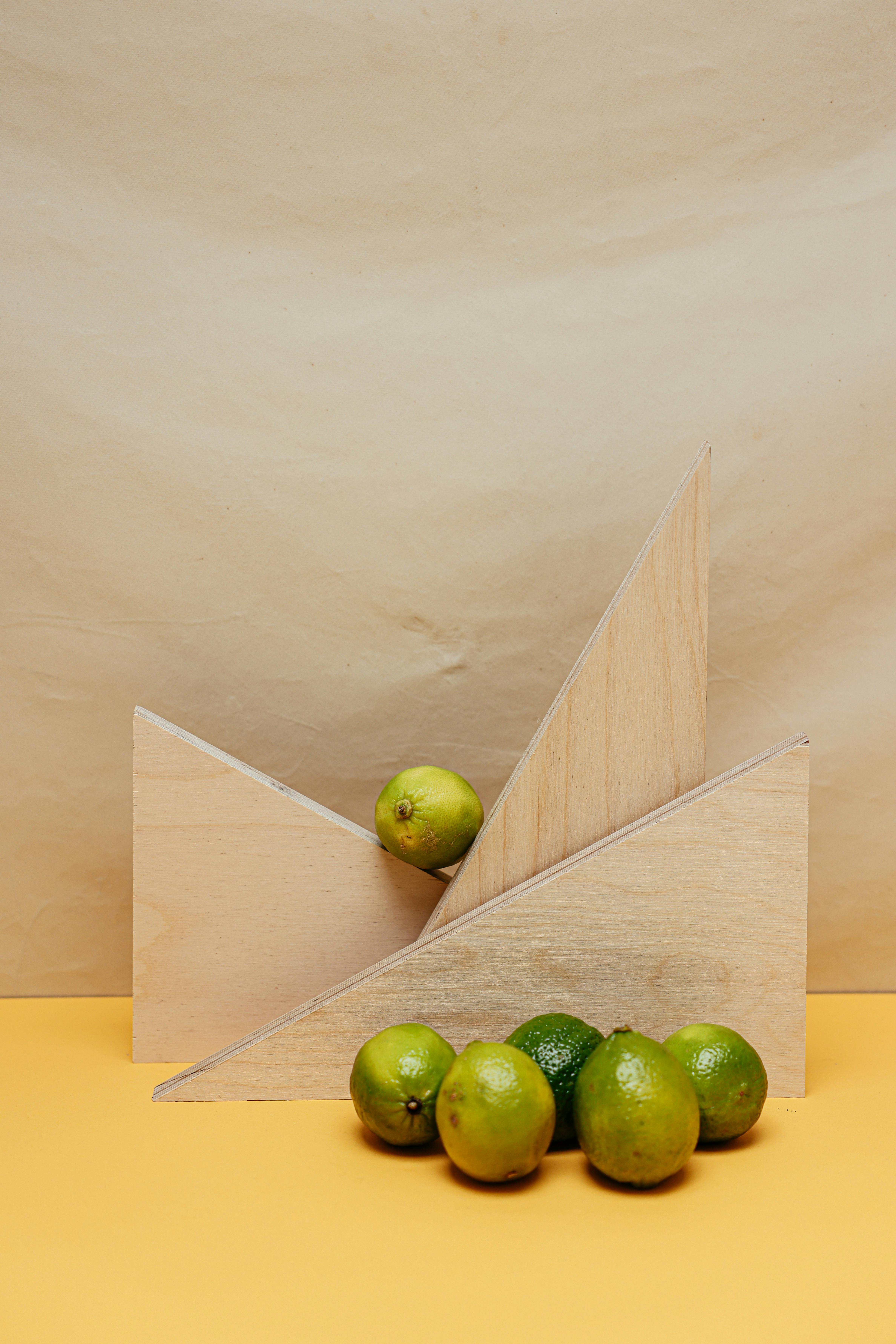 Creative still life with limes and geometric wooden shapes on yellow background.