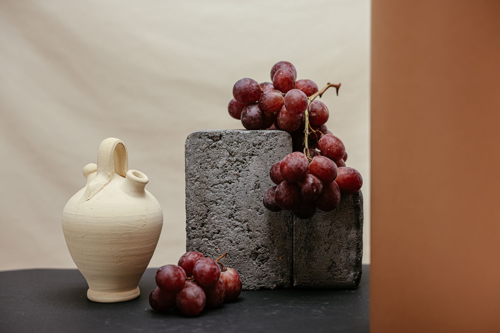Red Round Grapes on Gray Concrete Blocks Beside a White Ceramic Vase