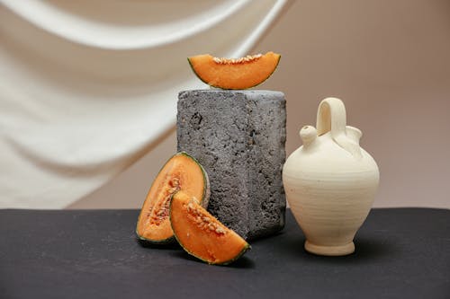 A Photograph of Sliced Melons Beside a Concrete Block and a Clay Pot