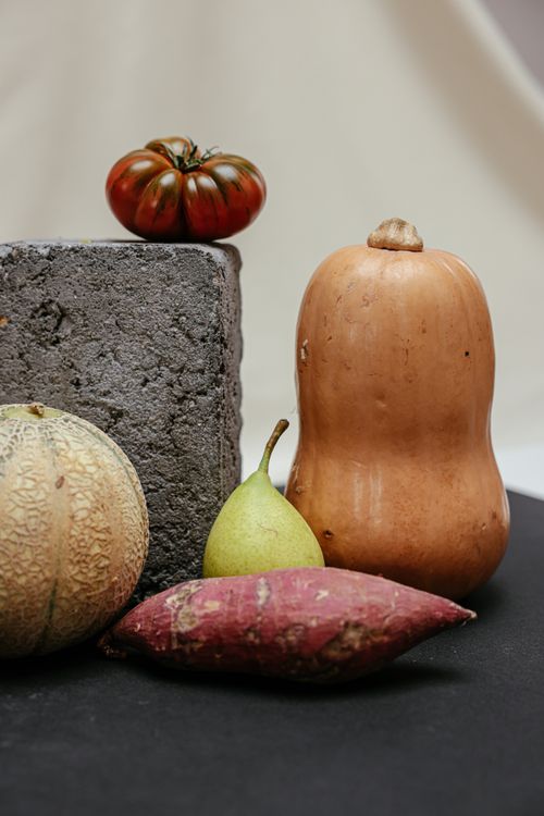 Free A still life featuring a variety of autumnal produce including squash, pear, and tomato against a rustic concrete block. Stock Photo