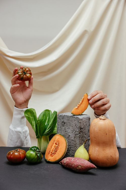 Free Hands holding vegetables and fruits in a creative display with a neutral backdrop. Stock Photo