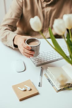 A cozy office desk setup with coffee, tech gadgets, and white tulips.