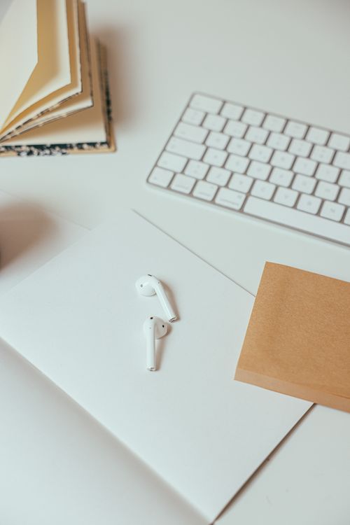 Free A clean, organized workspace featuring wireless earphones, a keyboard, and notepad on a white desk. Stock Photo