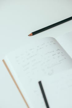Close-up of a handwritten notebook and pencil on a white surface, minimalist style.