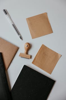 Elegant flat lay of stationery with notepads, pen, and stamp on a white surface.