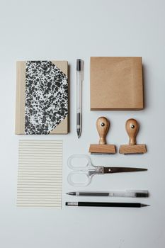 Top view of neatly arranged office supplies including notepad, pens, and stamps on white background.