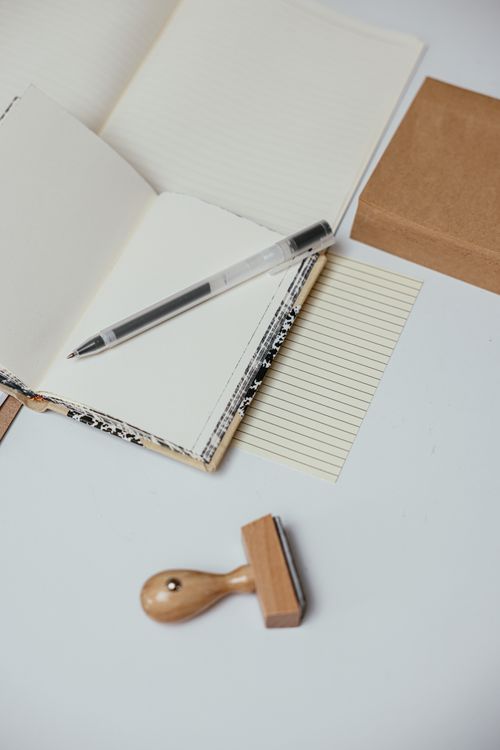 Free A minimalist workspace featuring an open notebook, pen, and wooden stamp on a white surface. Stock Photo
