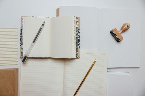 Free Flat lay of stationery items including notepads, pens, and a stamp on a white background. Stock Photo