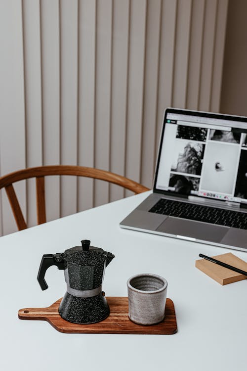 Coffee Maker and an Earthenware Cup on a Wooden Chopping Board 