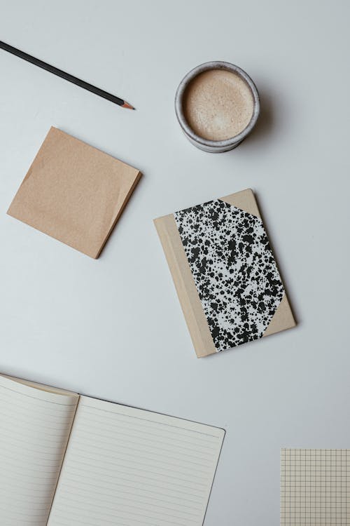 Top View of a Cup of Coffee, Notebooks and Sticky Notes Lying on White Surface