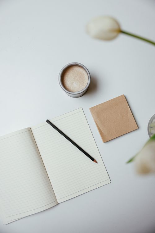 Free A top view of a minimalist workspace with a notebook, pencil, coffee, and flowers. Stock Photo