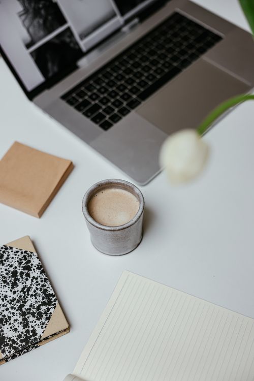 Free Top-down view of a minimalist workspace featuring a coffee cup, laptop, and notebooks on a white surface. Stock Photo