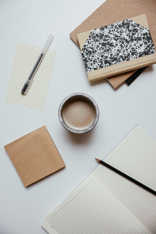 Free Minimalist flat lay of a coffee cup, notebooks, and stationery on a clean white desk. Stock Photo