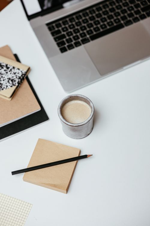 Free A clean workspace with a cup of coffee, a laptop, and notepads on a white surface. Stock Photo