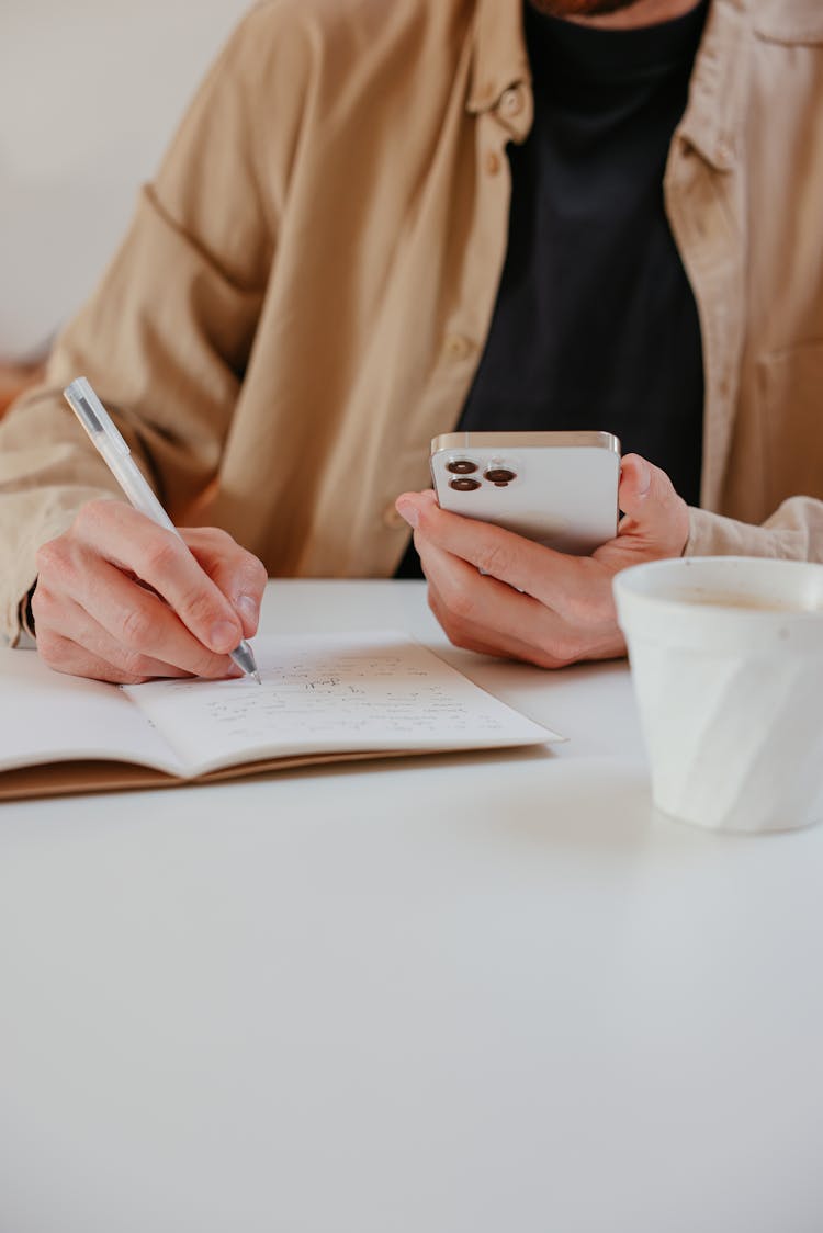 A Person Writing On A Notebook