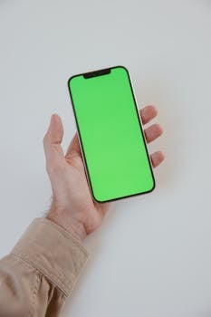 Close-up of a hand holding a smartphone with a green screen, ideal for mockup and design presentations.