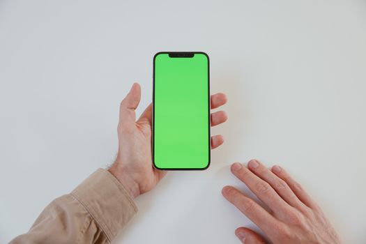 A person holding a smartphone with a green screen on a white surface, ideal for mockups.