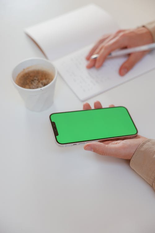 Free Close-Up Shot of a Person Holding a Smartphone while Writing Stock Photo