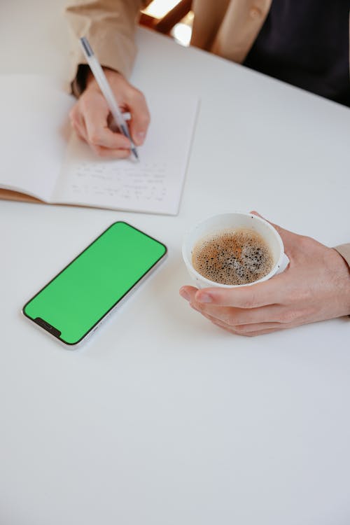 Close-Up Shot of a Person Holding a Cup of Coffee while Writing