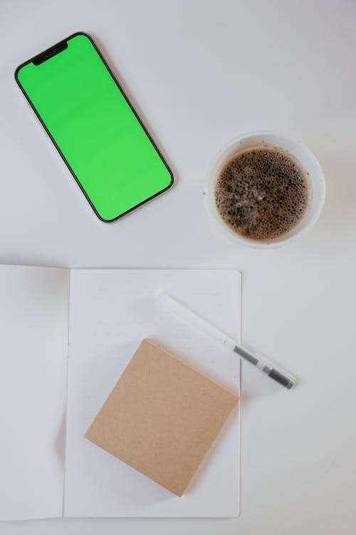 Free Close-Up Shot of a Smartphone beside a Cup of Coffee Stock Photo