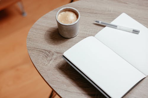 A Notebook with Blank Pages Beside a Pen and Cup of Coffee