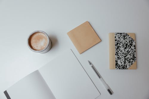 Close-Up Shot of Notebooks beside a Cup of Coffee