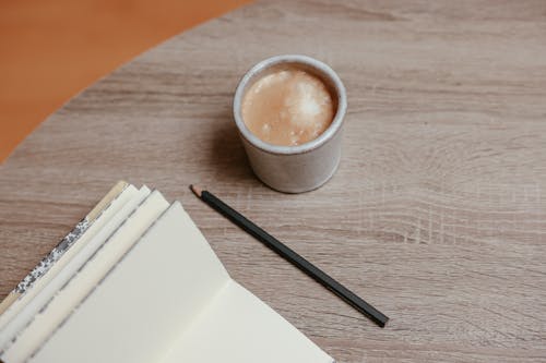 Black Pencil Beside Notepad and Cup of Coffee on Wooden Table