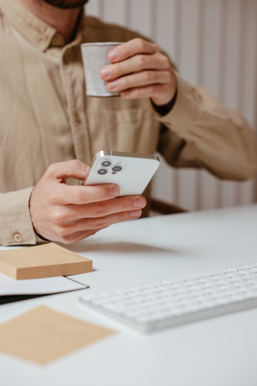 Free Close-up of a man using a smartphone and holding a cup in an office setting. Stock Photo