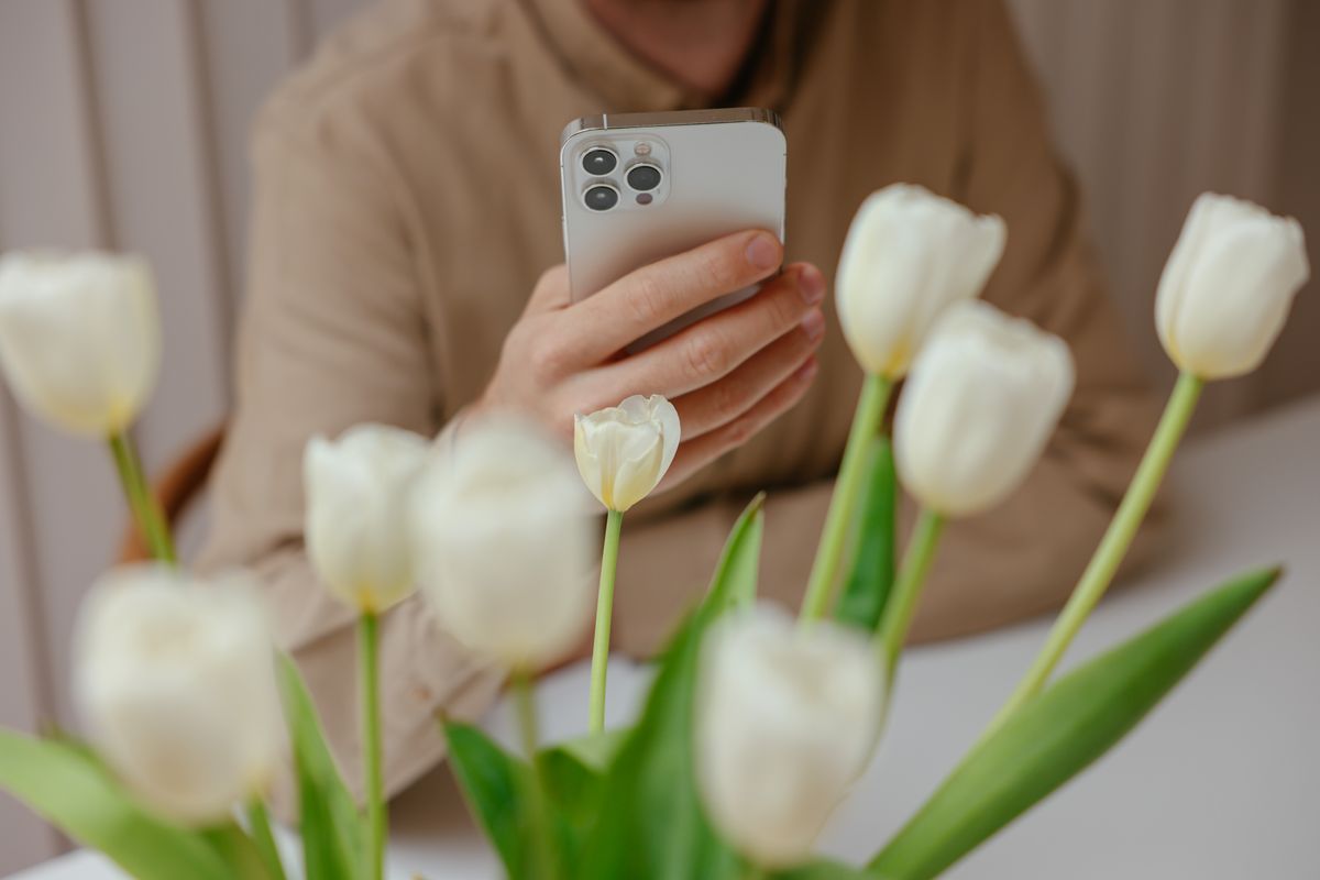 Bahar parkında akıllı telefon tutan genç bir kişi gülümsüyor