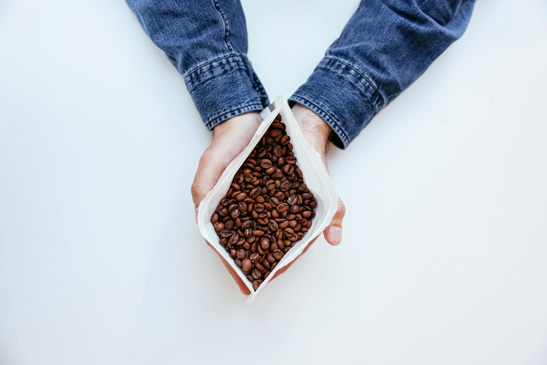 A Person in Blue Denim Jeans Holding a Plastic Pack with Coffee Beans