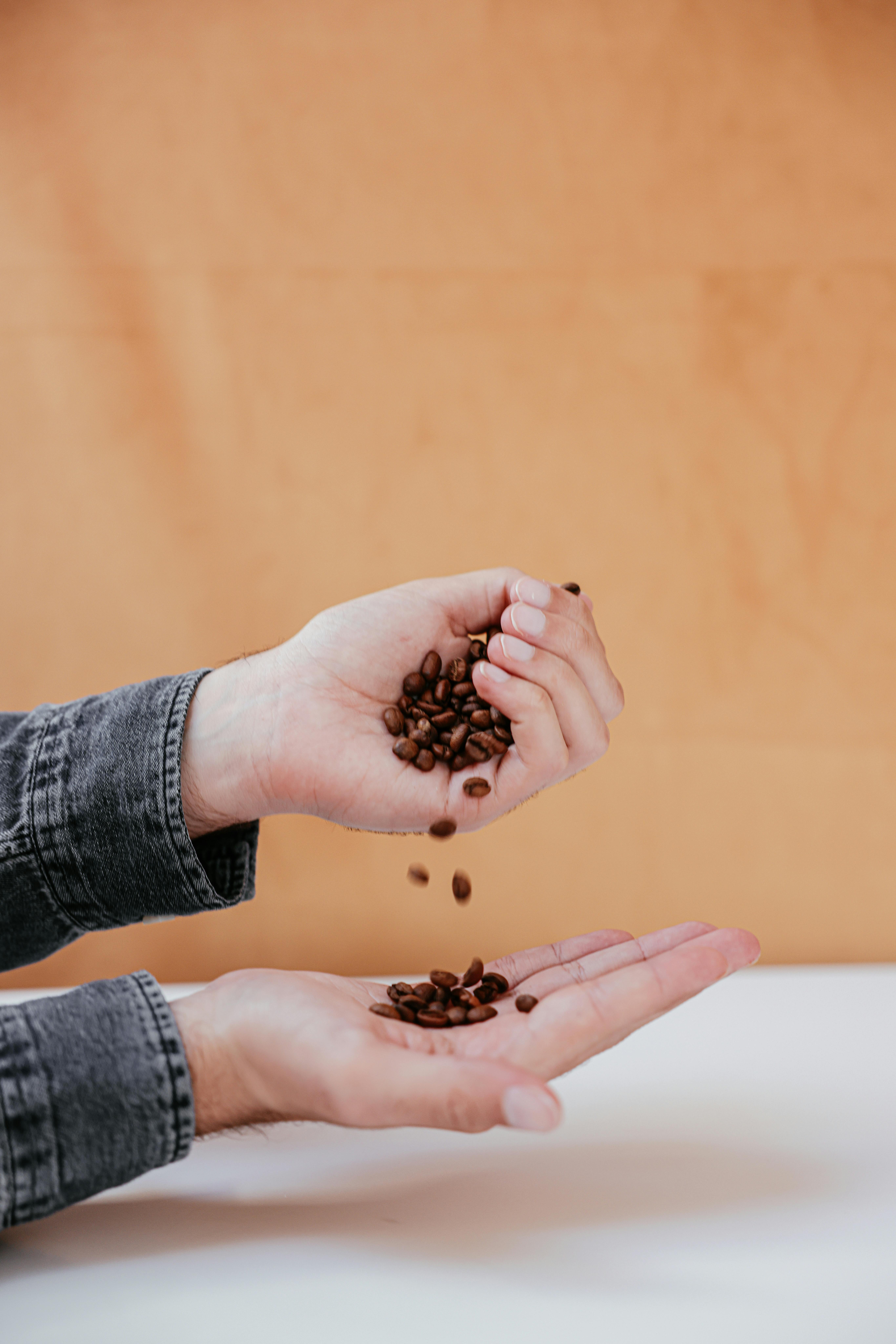 Close-up of hands pouring coffee beans against an orange backdrop.