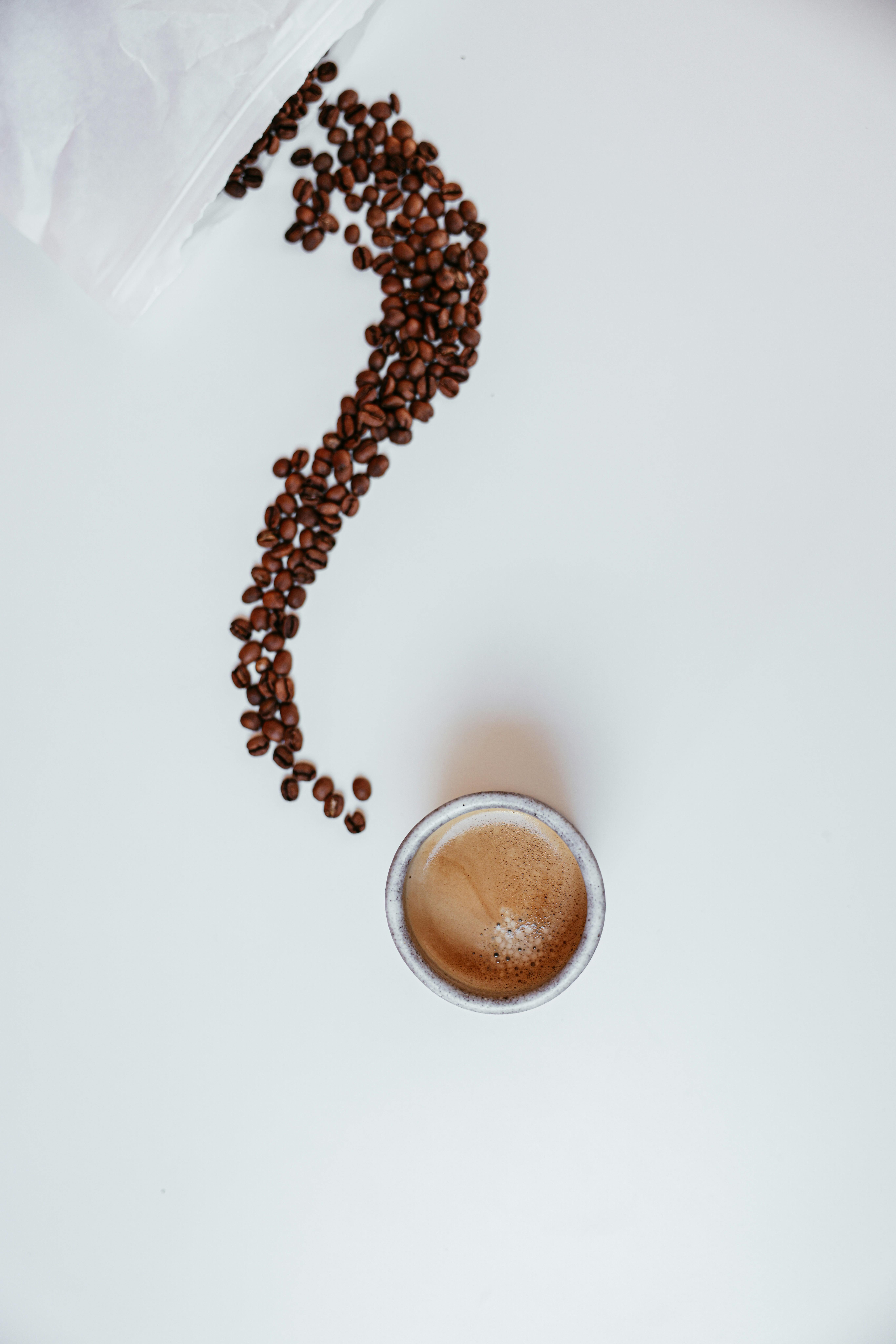 Cup of coffee with scattered beans forming a question mark on white background.