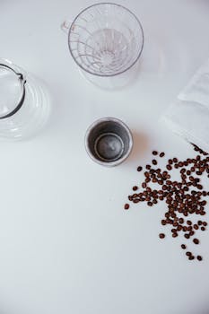 A minimalist coffee setup with beans, a mug, and a dripper on a white surface.