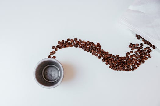 Top view of scattered coffee beans and a cup on a minimalist white table, perfect for modern art concepts.