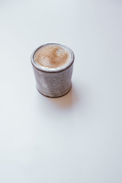 Free A minimalist ceramic coffee cup filled with frothy coffee on a clean white surface. Stock Photo