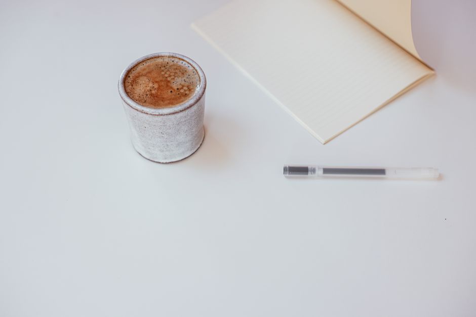 Patreon vs Buy Me a Coffee vs Ko-fi: Membership Features Compared (2024) A minimalist workspace setup featuring a cup of coffee, notebook, and pen on a white surface.