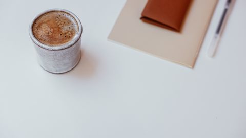 A minimalist setup with a cup of coffee, a notebook, and a pen on a white tabletop.