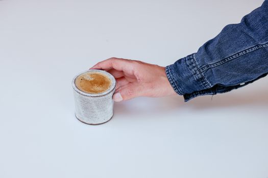 A cozy ceramic cappuccino cup being picked up on a white background.