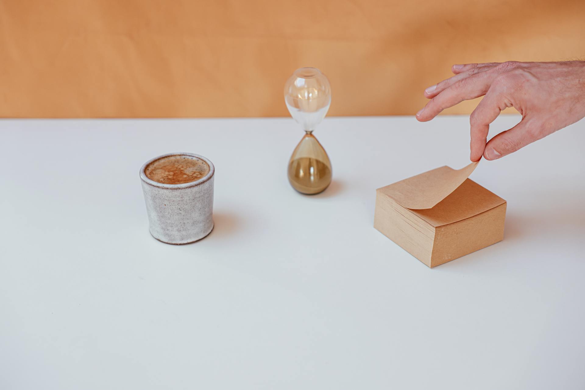 A minimalist desk setup featuring an hourglass, coffee cup, and notepad for time management inspiration.