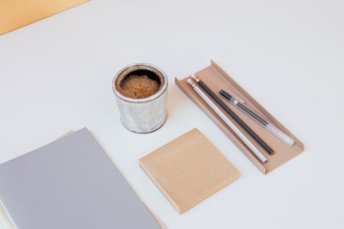 A Cup of Black Coffee Beside a Notepad and Pencils