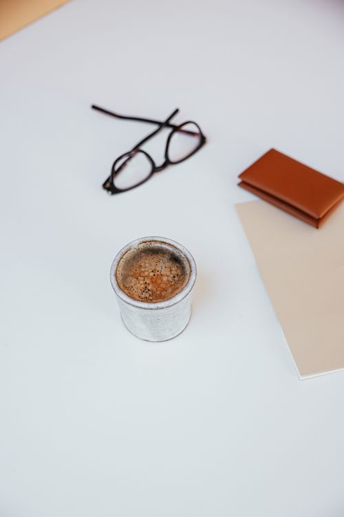 Free A minimalist flat lay of a coffee cup with eyeglasses and a notebook on a white surface. Stock Photo