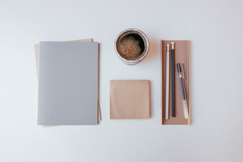 Free Flat lay of a minimalist workspace featuring coffee, notebooks, and stationery on a white background. Stock Photo