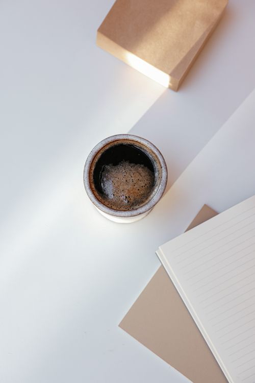 Free A warm cup of coffee with notebooks on a white background, perfect for productivity themes. Stock Photo