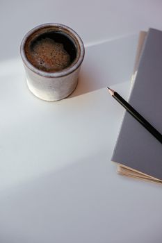 A minimalist setup of a coffee cup and a notebook on a white desk, perfect for work or study inspiration.