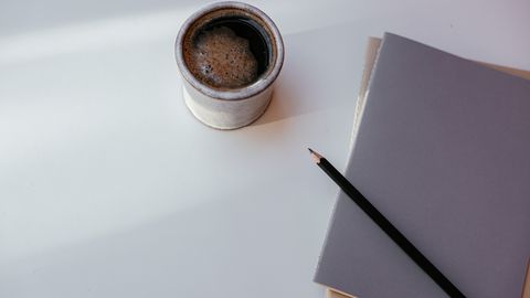 A cozy coffee mug with a notebook and pencil on a clean, minimalist desk.