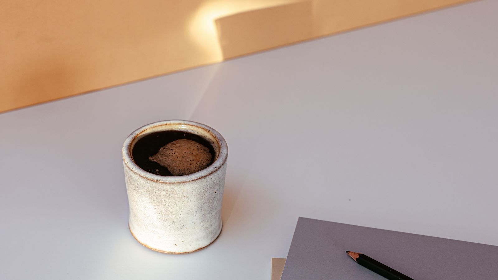 A ceramic coffee cup beside notebooks and a pencil on a sunlit table